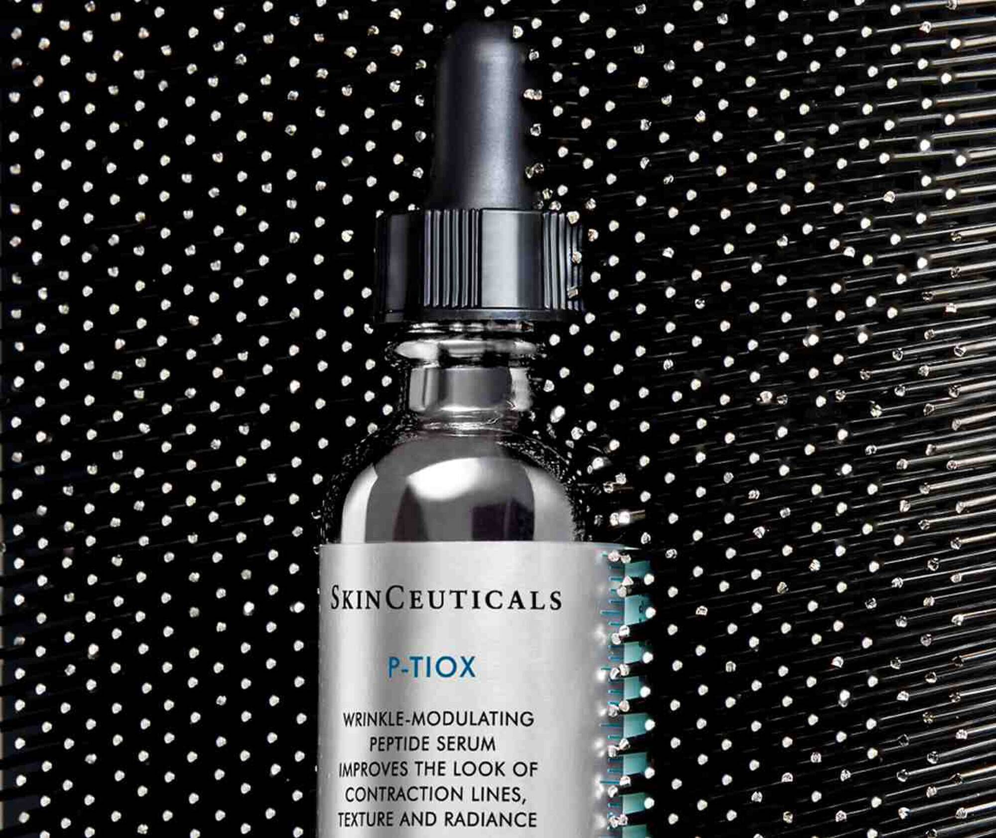 Ein Flaschchen SkinCeuticals P-TIOX Peptidserum vor einem schimmernden, reflektierenden Hintergrund.