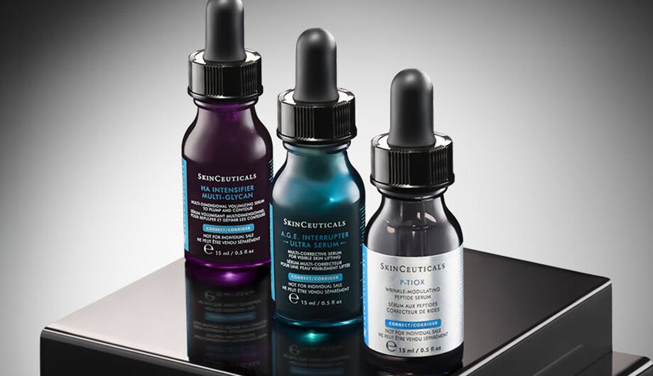 Eine Nahaufnahme von drei SkinCeuticals Hautpflegeprodukten: einem C E Ferulic Serum, einer A.G.E. Interrupter Advanced Creme und einem Advanced Brightening UV Defense Sunscreen SPF 50, die sich alle auf einer dunklen Oberflache spiegeln.​