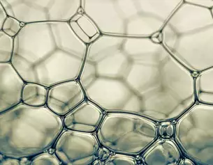 Detailaufnahme von Seifenblasen mit hexagonalen Strukturen und transparenten Blasen in sanften Farben.