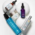Funf Hautpflegeprodukte von SkinCeuticals auf weißen runden Objekten, darunter Seren, eine Creme und ein Reinigungsmittel.