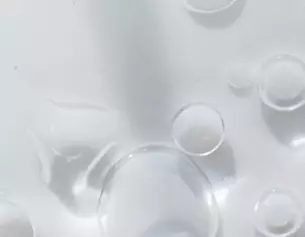Wassertropfen auf einer glatten, weißen Oberflache, schimmern und reflektieren das Licht.