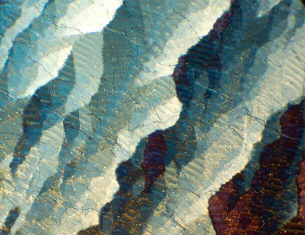 Nahaufnahme eines mineralischen Musters mit geschichteten Farben in Blau, Weiß und Rot, die Licht reflektieren.