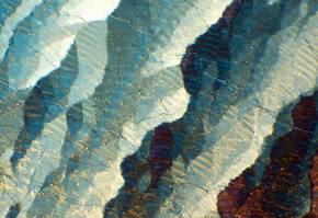 Nahaufnahme eines mineralischen Musters mit geschichteten Farben in Blau, Weiß und Rot, die Licht reflektieren.