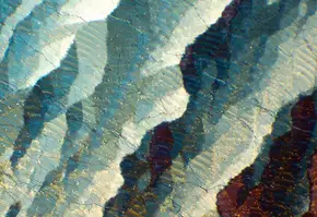 Mikroskopaufnahme von mineralischen Strukturen mit schimmernden Farbschichten und texturierten Formen.