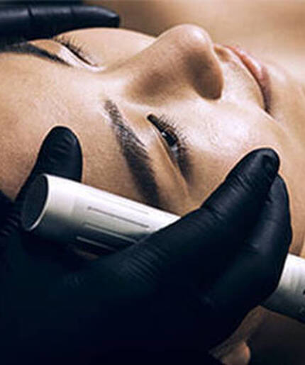 A person receiving a microneedling treatment at a spa, with a professional using a device on their face.