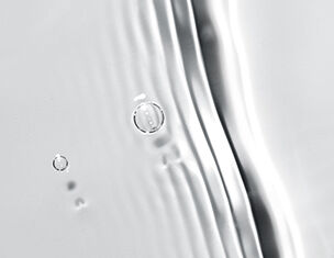 Wassertropfen gleiten an einer glatten, reflektierenden Oberflache entlang, erzeugen sanfte Wellen und Lichtspiele.