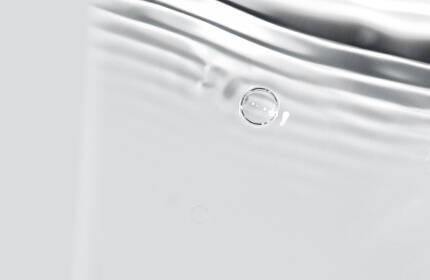 A close-up of rippling water with soft reflections and subtle bubbles, creating a serene and smooth texture.