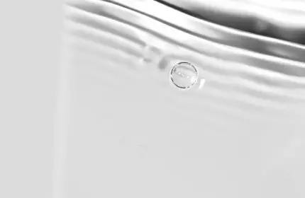 A close-up of rippling water with soft reflections and subtle bubbles, creating a serene and smooth texture.