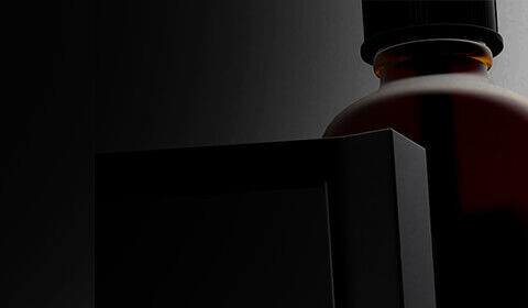 A close-up of a dark bottle and a stylized black object, set against a light gray background. The focus is on the unique shapes and textures.