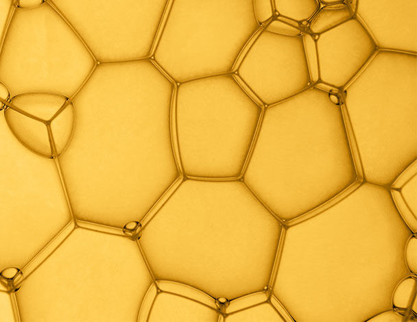 Nahaufnahme von schaumartigen Blasen in verschiedenen Großen, die eine goldene Farbe aufweisen.