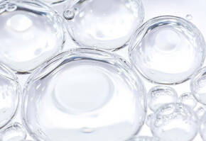 Klare Blasen und Wassertropfchen schweben auf hellem Hintergrund, wirken frisch und leicht.