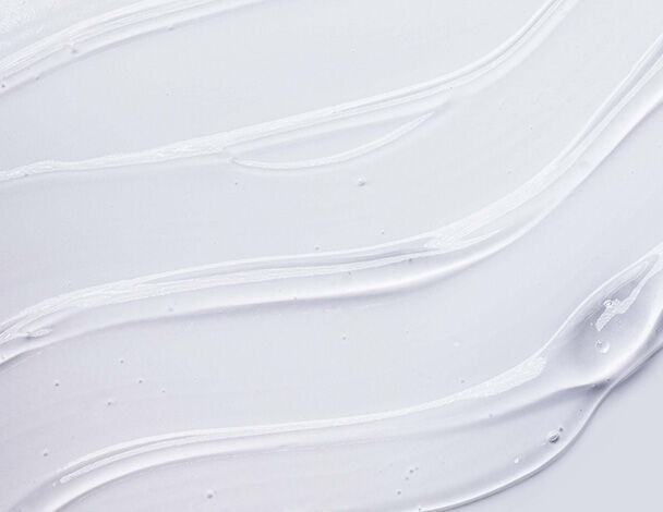 Close-up of smooth, creamy white lotion swirled on a light background, showcasing its glossy texture and sheen.