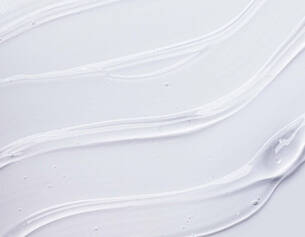 Close-up of smooth, creamy white lotion swirled on a light background, showcasing its glossy texture and sheen.