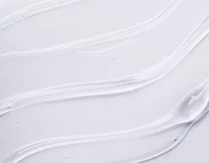 Close-up of smooth, creamy white lotion swirled on a light background, showcasing its glossy texture and sheen.
