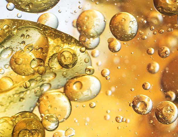 Nahaufnahme von goldenen Blasen und Tropfen in klarem Ol, das einen lebendigen, farbenfrohen Hintergrund schafft.