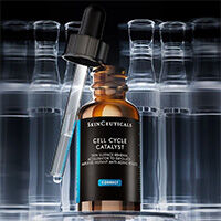 Im Fokus: die SkinCeuticals Cell Cycle Complex Serumflasche mit herausgezogenem Pipette, vor verschwommenen Flaschen im Hintergrund