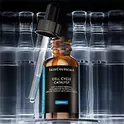 Im Fokus: die SkinCeuticals Cell Cycle Complex Serumflasche mit herausgezogenem Pipette, vor verschwommenen Flaschen im Hintergrund