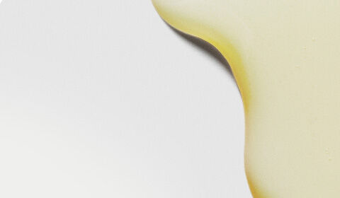 Close-up of smooth, yellow liquid droplets on a light background, creating an abstract pattern.