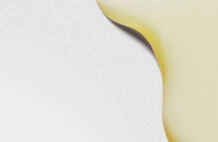 Close-up of smooth, yellow liquid droplets on a light background, creating an abstract pattern.