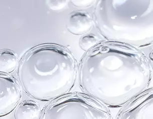 Nahaufnahme von klaren Wassertropfen, die auf einer glatten Oberflache liegen und Licht reflektieren.