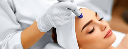 Eine Frau erhalt eine Gesichtsbehandlung in einem Schonheitssalon, wahrend eine Fachkraft ein Gerat auf ihre Stirn auftragt.