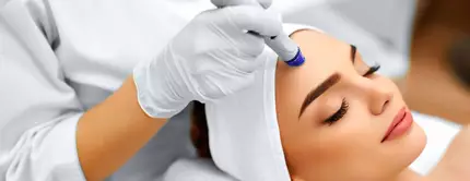 Eine Frau erhalt eine Gesichtsbehandlung in einem Schonheitssalon, wahrend eine Fachkraft ein Gerat auf ihre Stirn auftragt.