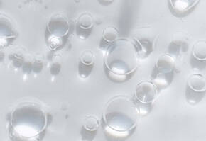 Nahaufnahme von Wassertropfen, die auf einer transparenten Oberflache verteilt sind und Licht reflektieren.