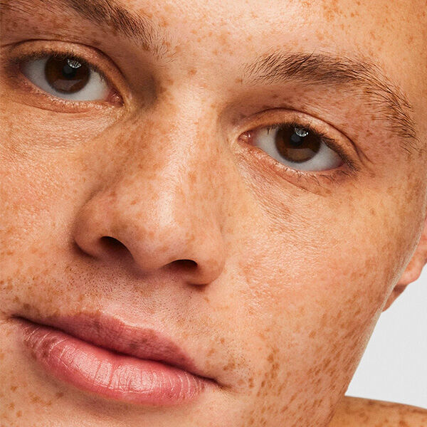 Close-up of a person's face with freckles, showcasing their expressive eyes and smooth skin texture.