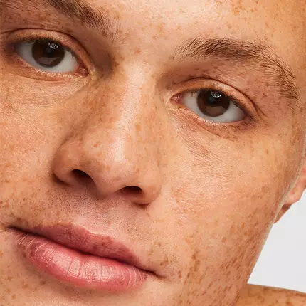 Close-up of a person's face, highlighting their light brown skin with freckles, expressive brown eyes, and a neutral expression.