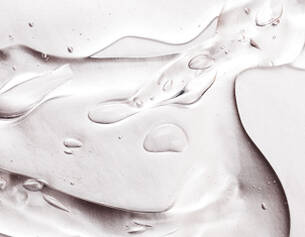 Close-up of a translucent gel with droplets, creating a smooth, flowing texture on a light background.