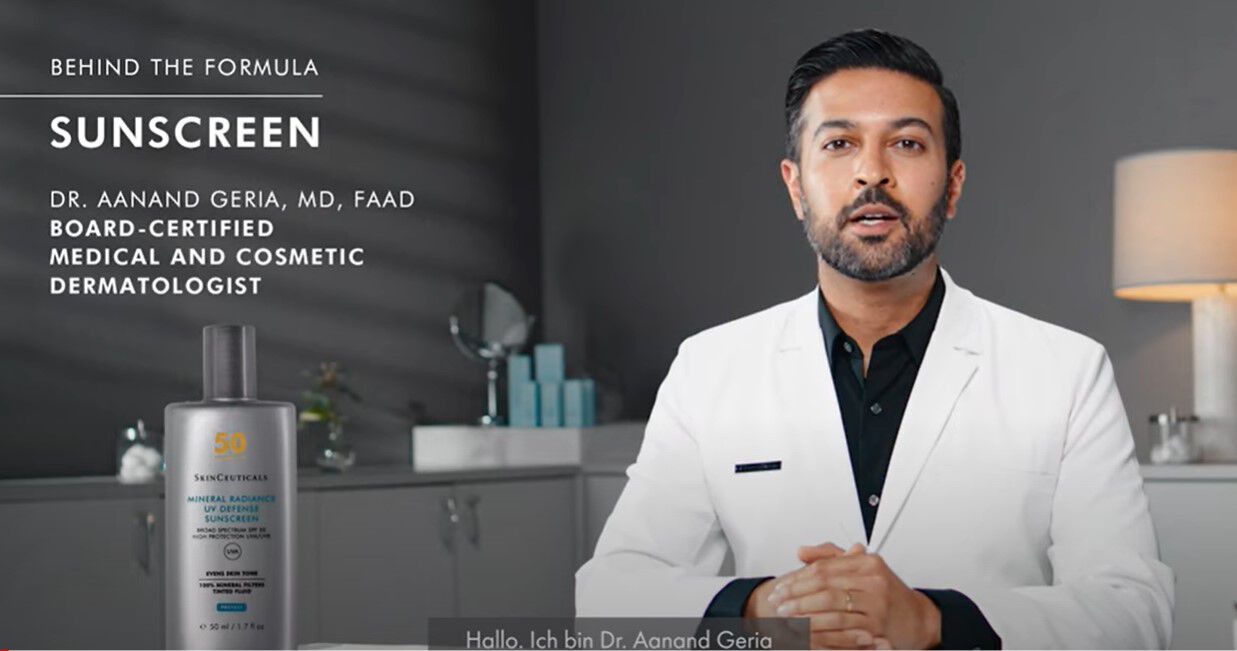A medical professional in a white lab coat introduces a sunscreen product, standing in a clinical setting with a bottle of the sunscreen displayed on a table beside them.
