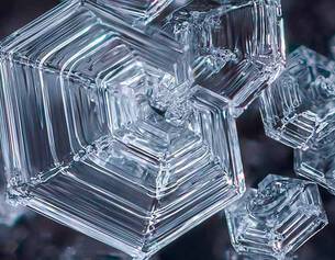 Close-up of intricate, transparent ice crystals showcasing geometric, hexagonal shapes against a dark background.