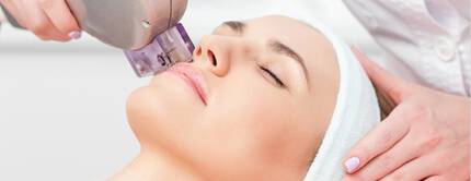 Eine Frau erhalt eine Gesichtsbehandlung mit einem Hautbehandlungsgerat. Sie hat die Augen geschlossen und sieht entspannt aus.