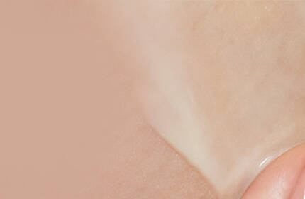 A close-up of a hand gently applying a creamy skincare product to smooth skin with a soft, neutral background.